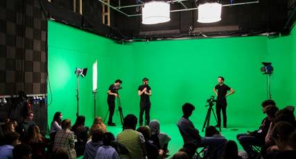Film students stood recording in front of a green screen to an audience