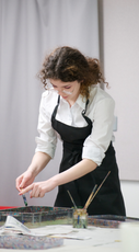 A young person, who is wearing an apron, tapping a brush