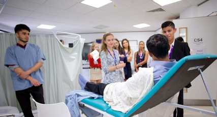 Medicine students performing a role play task where one student is laid on a GP’s bed while others interact with him