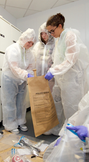 Forensic science students in overalls putting evidence into a bag
