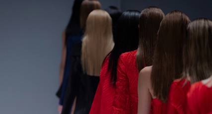 A group of fashion design students wearing their designs with their backs to the camera