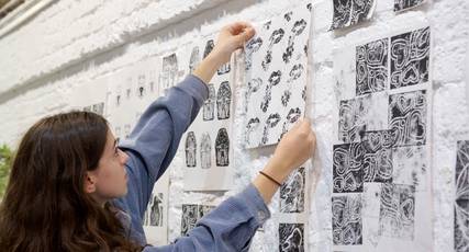 A young person holding their artwork against a wall