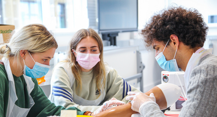  Medicine students performing practical work on a mannequin hand